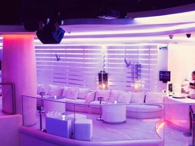 Interior de la discoteca Pacha Barcelona: zona VIP con mesas iluminadas, sofás blancos y luces rojas y púrpuras. El ambiente es nocturno, con decoración moderna y elegante, y la pista de baile se ve al fondo bajo focos y efectos de luz