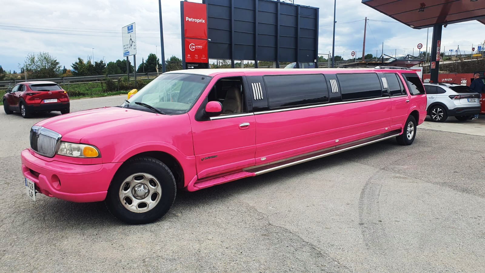 Limusina vista de lado con gasolinera de fondo