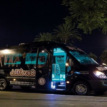 Minibús negro estacionado en una calle de Barcelona, con capacidad para 17 personas y una puerta lateral de color azul.