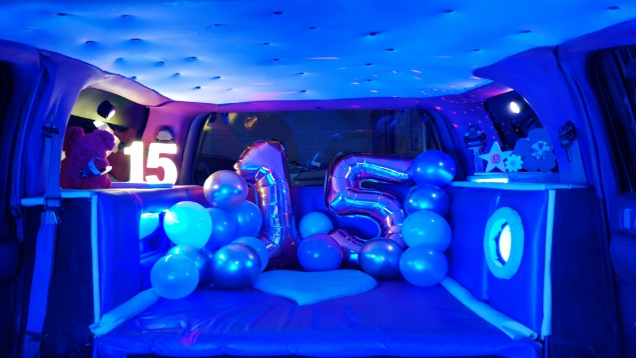 Interior de una limusina Hummer rosa, decorada para un cumpleaños, con asientos de cuero, iluminación LED de colores y adornos festivos que crean un ambiente de celebración.